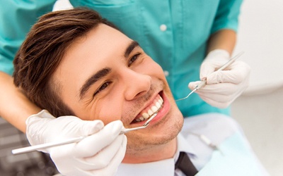 A dental hygienist cleaning a young man’s mouth