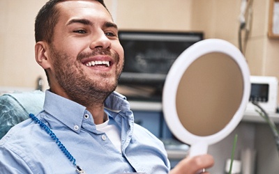 A man looking at his smile in the mirror at the dentist’s office