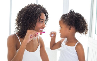 A mother and daughter at home brushing their teeth together
