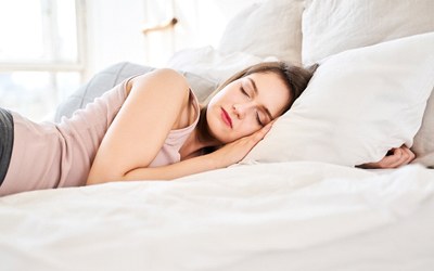 A young woman with dark hair sleeping with her head against a pillow at home